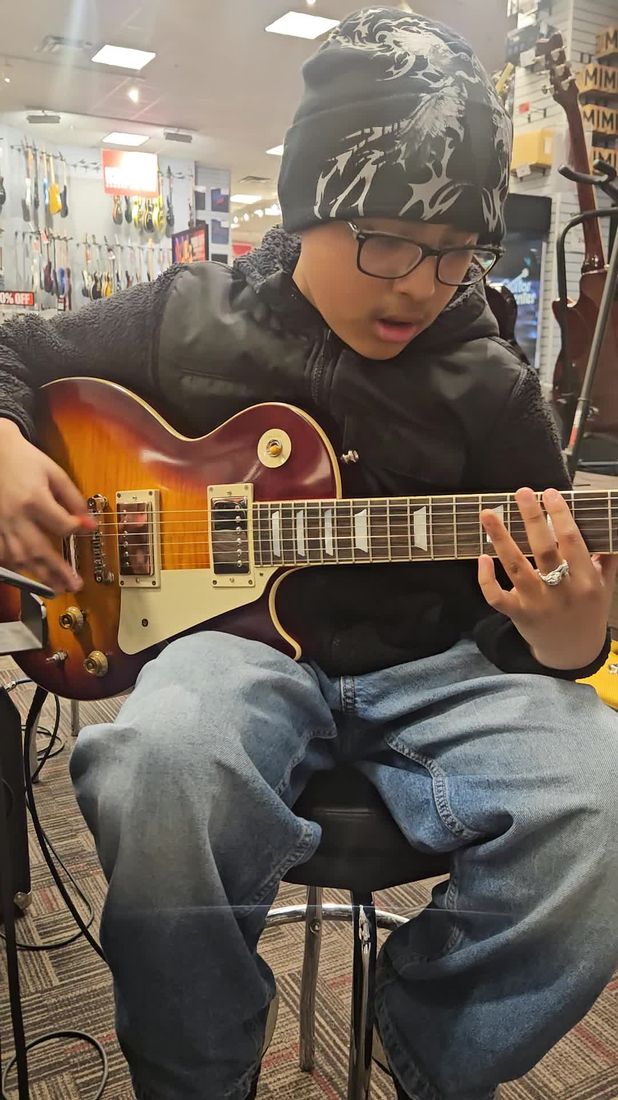 Alex playing a sunburst electric guitar at a music store